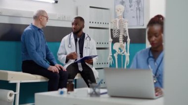 Genel pratisyen hekim doktor muayenesinde yaşlı bir adama hastalık konusunda danışmanlık yapıyor. Sağlık uzmanı hastaya danışmanlık yapıyor, profesyonel tavsiyelerde bulunuyor..
