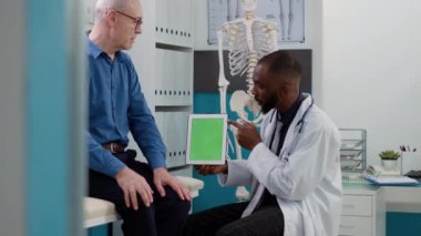 General practitioner holding greenscreen on tablet at checkup visit with male patient. Senior man and medic looking at blank copyspace display with chroma key background and isolated template.