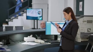 Sağlık çalışanı kontrol formlarını analiz ediyor ve hastane kayıt gişesinde sağlık randevuları alabilmek için raporlar hazırlıyor. Lobideki resepsiyonda çalışıyor. El kamerasıyla..