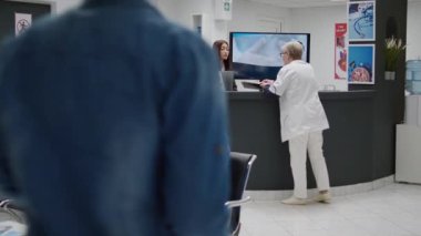 Asian receptionist working at hospital reception counter, helping doctor with appointments and patients. Medical worker preparing healthcare consultations and checkup visits in waiting area.