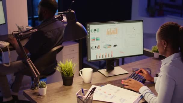 オフィスワーカーは オンライン情報を使用してコンピュータネットワーク上の研究データを分析し ビジネスレポートを作成します 夜遅くにオフィスでチャート付きのWebプレゼンテーションノートの作業 — ストック動画