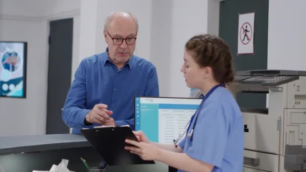 Asystentka Medyczna Dawny Pacjent Wypełniają Papiery Kontrolne Recepcji Szpitala Pielęgniarka — Wideo stockowe