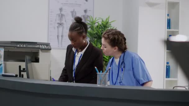在医院接待处工作的各种医疗小组 帮助病人安排检查时间和报告文件 护士和接待员坐在设施前厅登记台 — 图库视频影像