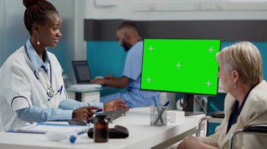 Kadın sıhhiyeci ve felçli hasta yeşil ekran analizi yapıyor, izole edilmiş krom anahtar şablonu ve boş model geçmişi kullanıyor. Tekerlekli sandalyedeki engelli kadın, boşluğa bakıyor..