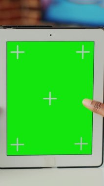 Dikey video: İzole edilmiş ekranda yeşil ekranı analiz eden genç yetişkin, boş arkaplan ile dijital tableti dikey olarak tutuyor. Taşınabilir modern aygıttaki kroma anahtar ekranına ve kopyalama alanına bakılıyor