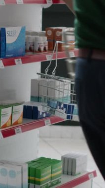 Dikey video: Raflardaki tıbbi ürünlere ve ilaçlara bakan genç yetişkinler, paketlerdeki ilaç ve tedavileri satın alıyorlar. Eczane almak için eczaneye, perakende satış mağazasına gidiyorum..