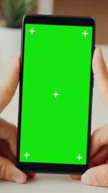 Dikey video: Akıllı telefon uygulamasında yeşil ekran görüntüsüne bakan erkek serbest yazar, izole edilmiş arka plan ve model şablona sahip telefon kullanıyor. Boş krom anahtar kopyalama alanına bakıyorum. Kapatın. Üçayak