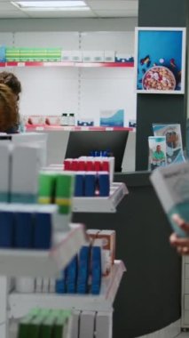 Dikey video: Kadın eczacı eczane tezgahındaki Asyalı müşteriye reçeteli ilaç ve takviyelerden bahsederek sağlık ürünlerini açıklıyor. Eczane masasında uyuşturucu paketi bulundurmak..