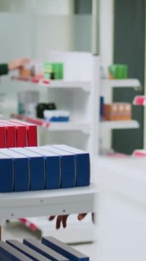 Dikey video: Afro-Amerikalı kadın vitamin broşürleri okuyor ve eczane raflarından ilaç paketini kontrol ediyor. Eczaneden ilaç ve hap almak için ilaç ürünlerine bakıyorum..