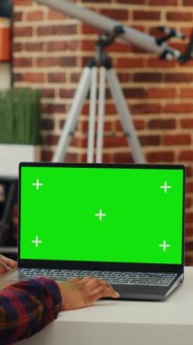 Dikey video: Laptop 'ta yeşil ekran görüntüsüne bakan bayan çalışan, kablosuz bilgisayarda izole edilmiş boş maket şablonu kullanıyor. Ana masadaki krom tuşlu kopya alanı arka planında çalışan kadın.