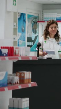 Dikey video: Tıp çalışanı eczane tezgahındaki ilaç kutularını tarıyor, müşterilere ilaç ve ilaç almalarında yardımcı oluyor. Eczane masasında vitamin takviyeleriyle çalışan bir çalışan..
