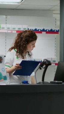 Dikey video: Eczacı üst düzey müşteriyle kardiyoloji hapları hakkında konuşuyor, ilaç kutusunu tarıyor ve eczane masasında çalışıyor. Tıp çalışanı, reçetedeki vitamin ve takviyeleri açıklıyor