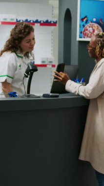 Dikey video: Afrikalı Amerikalı bir kadın eczacıya almak için ilaç paketlerini soruyor, reçeteli ilaçlardan ilaç bulmaya çalışıyor. Sağlık ürünleri arayan kadın müşteri.