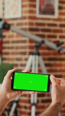 Dikey video: Cep telefonunda yatay yeşil ekran görüntüsünü kontrol eden erkek çalışan, izole krom anahtar şablonlu akıllı telefona bakıyor. Boş kopyalama arkaplanı ile çalışmak.