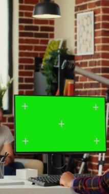 Dikey video: Masaüstü bilgisayarında boş kroma anahtar şablonu kullanarak yeşil ekran ile bilgisayarı analiz eden çeşitli personel ekibi. Arka planda izole edilmiş bir kopyalama alanı görüntüsüyle çalışan kadın ve erkek