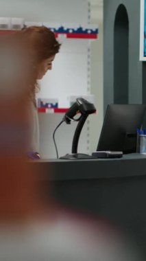 Dikey video: Eczane tezgahında ilaç kutularını tarayan kadın eczacı, müşterilere ilaç ve ilaç almaları için yardım ediyor. Eczane masasında ilavelerle çalışan bir çalışan..