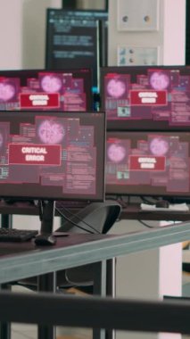 Dikey video: Ekranda sistem çökmesi uyarısı, ekranda kritik hata mesajı gösteren birden fazla monitörü olan boş bir ajans ofisi. Masada güvenlik ihlali gösteren bilgisayarlar.
