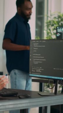 Dikey video: Terminal pencere üzerinde html betiği ile çalışan sistem mühendisi, bilgisayar ekranına ve daktiloya bakıyor. Ofisteki yazılım geliştiricisi ai algoritması ve sistemi yeniliyor