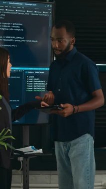 Dikey video: Yazılım programcıları büyük ekrandaki ve tabletteki algoritmalardan bahsederek html betik dilini analiz ediyorlar. Sistem mühendislerinden oluşan bir ekip terminal penceresinde, sunucuda veritabanını tartışıyor