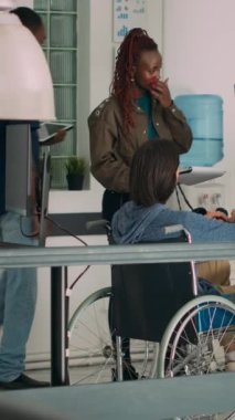 Dikey video: Ajans ofisinde yazılım kodu üzerinde çalışan Asyalı programcı. Geçici pencere üzerinde html betiği kullanarak tekerlekli sandalyede engelli uygulama geliştiricisi.