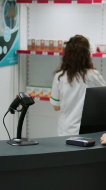 Dikey video: Eczane masasında ilaçların parasını ödeyen Asyalı müşteri, reçeteli ilaç ve kardiyoloji hapları almak için NFC ödemesini kullanıyor. İlaçlar ve vitaminler alınıyor..