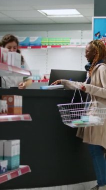 Dikey video: Genç müşteri reçeteli tedavi, ilaç ve ilaç paketleri almak için eczane raflarından kutu kutu hap alıyor. Eczacıya vitaminleri soruyordum. Üçayak