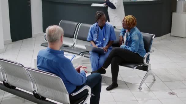 Медицинский Ассистент Показывает Диагностику Заболевания Ноутбуке Молодому Пациенту Сидящему Приемной — стоковое видео