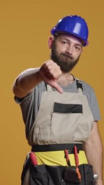 Dikey video: Stüdyoda onaylamayan ve anlaşmazlık gösteren inşaat işçisinin portresi. Sevmediğiniz jestler ve olumsuz ciddi işaretler yapmak, inşaatçının çatışma içinde olması.
