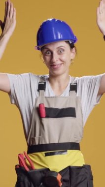 Dikey video: Güçlü tamirci kadın yukarı yönde reklam vermek ve inşaat inşaatında çalışmak için yukarı işaret ediyor. Müteahhit, yukarıdaki stüdyoda ve mühendislik üniformasında reklam olduğunu belirtiyor..