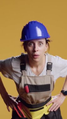 Dikey video: Kendine güvenen, meraklı ve araştırmacı davranan, sarı arka planda duran kadın portresi. Kadın müteahhit kameraya bakıyor ve aptalca davranıyor, araştırıyor ve araştırıyor.