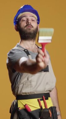 Dikey video: Boya fırçası kullanan işçilerin portresi ve yenileme ve yenileme üzerinde çalışmak için ödemeli boya rengi. Yeniden düzenleme için yeniden inşa araçları ve boyama ile çalışmak.