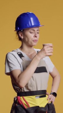 Dikey video: Güçlü inşaatçının portresi bir fincan kahve içmek, yenilenmeye ve stüdyodaki yenileme çalışmalarına ara vermek. Kadın müteahhit cappuccino ya da latte kafein içeceğini seviyor..