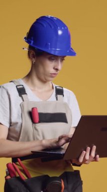 Dikey video: Bilgisayarda internette gezinen kendine güvenen bir kadın, tipik bir inşaat işinde çalışmak için inşaat ilhamı arıyor. Stüdyoda bilgisayar kullanan, endüstriyel işler yapan bir kadın.