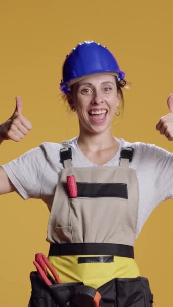 垂直录像 女建筑工人在工作室中抛出大拇指的肖像 在镜头前表示认可和同意 女建筑工人做得喜欢和满意的姿态 好的装修工作 — 图库视频影像