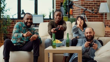 Bir grup insan konsolda video oyunları oynuyor, televizyonda oyun yarışmasının keyfini çıkarıyorlar. Sosyal buluşmada bira eşliğinde oyun oynamak eğlenceli oluyor. Üçayak atışı.