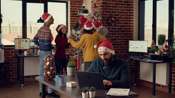 紧张的男人被快乐的同事们打断了 他们用圣诞装饰品庆祝办公室里的寒假 圣诞节前夕 吵吵闹闹的人在骚扰人 — 图库照片
