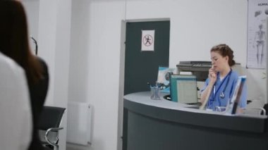 Kadın hemşire, sağlık merkezindeki resepsiyondaki sabit telefon görüşmelerine cevap veriyor. Tıbbi randevu almak için telefon hattını kullanıyor. Hastane kayıt gişesinde çalışıyorum. El kamerasıyla..