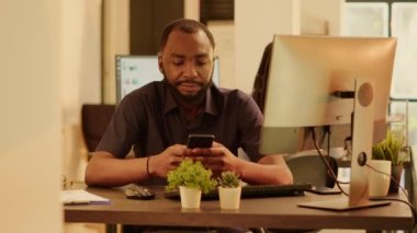 Portrait of african american man using smartphone app on computer, planning business presentation and doing research on social media network. Working with internet application on mobile phone.