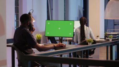 Startup worker analyzing greenscreen on monitor in office with big windows, looking at desktop isolated screen. Working with chroma key display, blank copyspace and mockup template. Tripod shot.