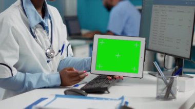 General practitioner showing horizontal greenscreen on tablet, meeting with patient wheelchair user. Using isolated chroma key template with blank mockup display and copyspace. Close up.