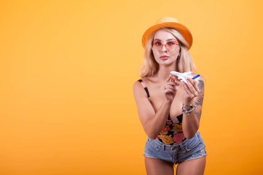 Genç kadın rahat kıyafetler oyuncak uçak ile sarı arka plan üzerinde oynarken