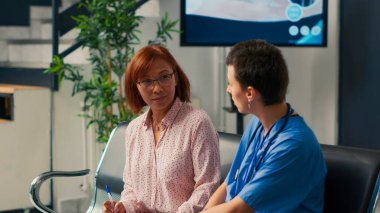 Sağlık asistanı hastanın sağlık raporunu doldurmasına, form doldurmasına ve danışmanlık randevusuna katılmasına yardım ediyor. Teşhis için Asyalı kadına danışmanlık yapan hemşire, sağlık tavsiyesi.