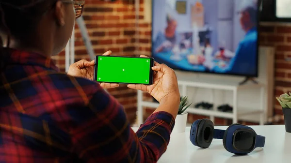 Office employee looking at horizontal greenscreen on smartphone, using mockup blank copyspace with chroma key on display. Holding telephone with isolated copy space template in apartment.