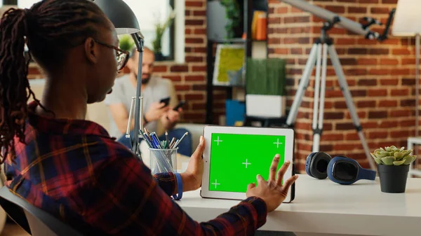 African american adult using portable tablet with horizontal greenscreen on display, analyzing blank copy space template on device. Looking at isolated background with chroma key.