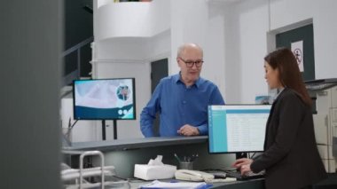 Eski bir hasta, Asyalı resepsiyonistle resepsiyonda tıbbi randevu almak için kredi kartı kullanıyor. Kontrol ve tedavi masraflarını ödeyen kıdemli bir adam. El kamerasıyla..