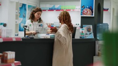 Eczane tezgahından ilaç ve tıbbi paketler alan Afrikalı Amerikalı bir müşteri eczacı ilaç ve tedavi satan bir eczacı. Eczanede ilaçların parasını ödeyen kişi. El kamerasıyla..