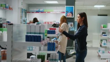 Gülümseyen Asyalı müşteri raflardaki ilaç paketlerini kontrol ediyor, eczaneden satın almak için sağlık ürünlerine bakıyor. Eczanede, eczanede kardiyoloji hapı okuyan kadın..