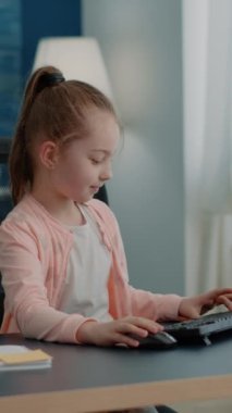 Dikey video: Öğrenci masadaki online ders için klavye ve bilgisayar kullanıyor. Okul ödevi ve ödevi için monitöre bakan genç bir kız. Uzaktan eğitim için bilgisayar üzerinde çalışan küçük bir çocuk ve