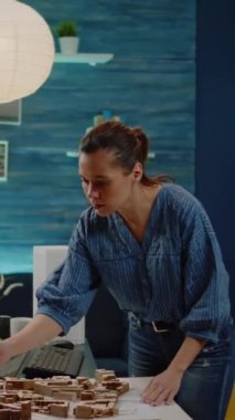 Dikey video: Kadın mimar modern binanın planlarını ve maket analiz modelini kontrol ediyor. Mimarlık ofisinde geliştirme projesi için kişi mühendisliği.