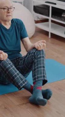 Dikey video: Nilüfer pozisyonundaki sakin emekli yoga minderinde rahatlamak için meditasyon yapıyor. Kıdemli adam refah ve rahatlama için meditasyon yapıyor. Ahenk için pilates yapan yaşlı bir insan..